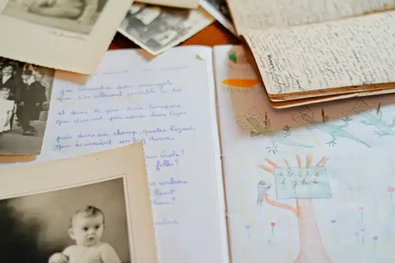 Fotografías familiares antiguas en blanco y negro junto a cartas y un cuaderno escolar escritos a mano en francés